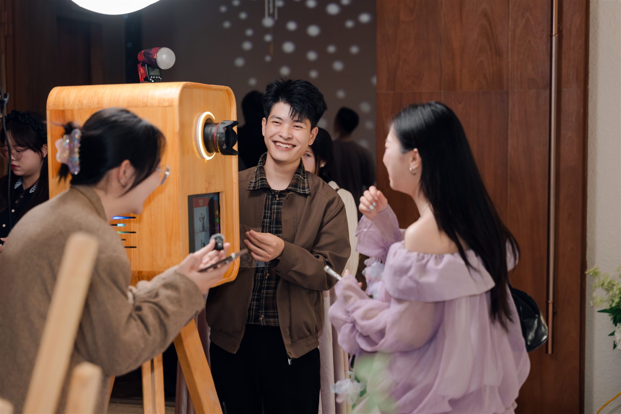 Khách mời cười rạng rỡ bên máy photobooth gỗ của HM với đèn vòng sáng tại tiệc cưới