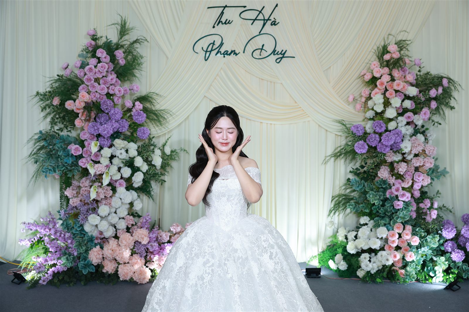 Cô dâu tạo dáng tại photobooth đám cưới với backdrop hoa